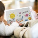 Back view of a parents and a toddler looking at a picture book with drawings of Saturn, a light bulb, etc., with the words FUN and LEARN