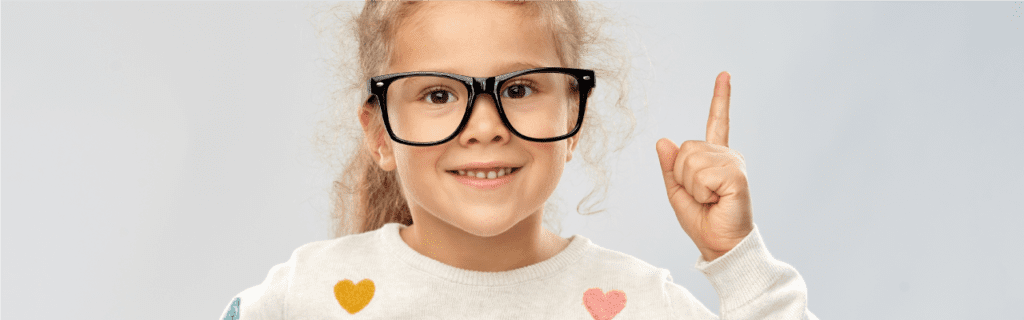 A happy Caucasian female child wearing black-framed spectacles and pointing up