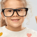 A happy Caucasian female child wearing black-framed spectacles and pointing up