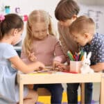 Four Caucasian kids gathered at a table, looking at a picture book